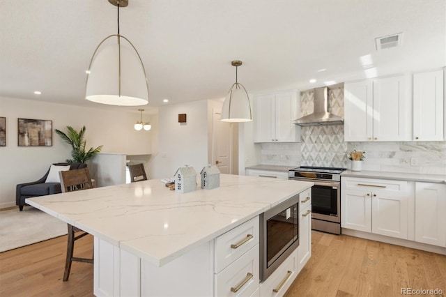 kitchen with appliances with stainless steel finishes, visible vents, light wood-style flooring, and wall chimney range hood