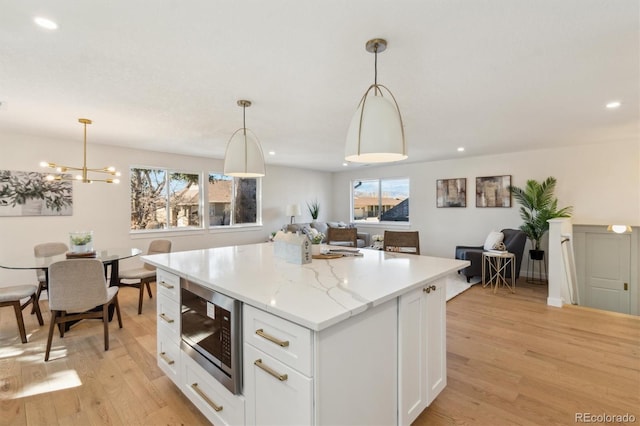 kitchen with a kitchen island, stainless steel microwave, a healthy amount of sunlight, light wood-style floors, and white cabinetry