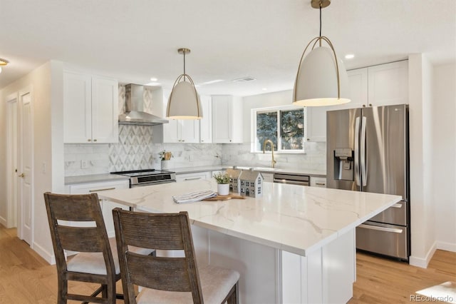 kitchen featuring stainless steel appliances, light wood-style floors, white cabinetry, a sink, and wall chimney exhaust hood