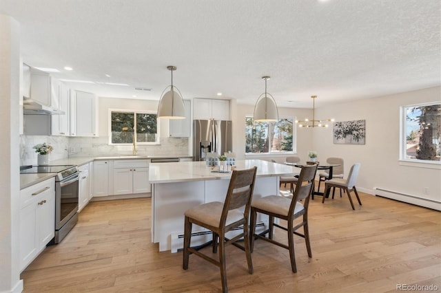 kitchen with a breakfast bar area, light wood-style flooring, a kitchen island, appliances with stainless steel finishes, and tasteful backsplash