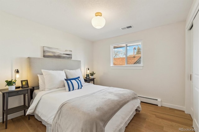 bedroom with visible vents, baseboards, light wood-style floors, baseboard heating, and a closet