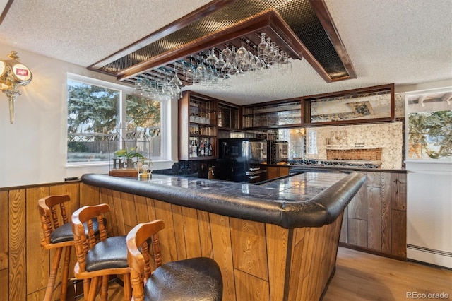 bar featuring a dry bar, light wood-style floors, wainscoting, a textured ceiling, and fridge