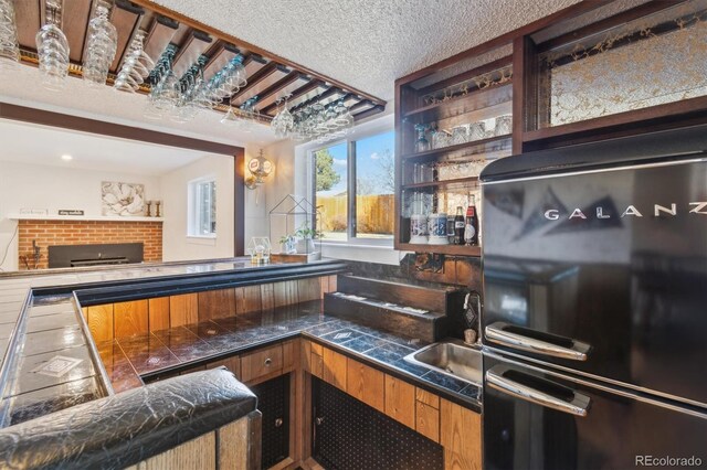 bar featuring a sink, a textured ceiling, indoor wet bar, and freestanding refrigerator