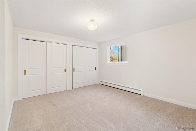 unfurnished bedroom featuring a baseboard heating unit, baseboards, carpet flooring, and multiple closets