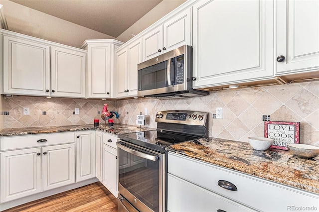 kitchen featuring stainless steel appliances, dark stone countertops, light hardwood / wood-style floors, decorative backsplash, and white cabinets