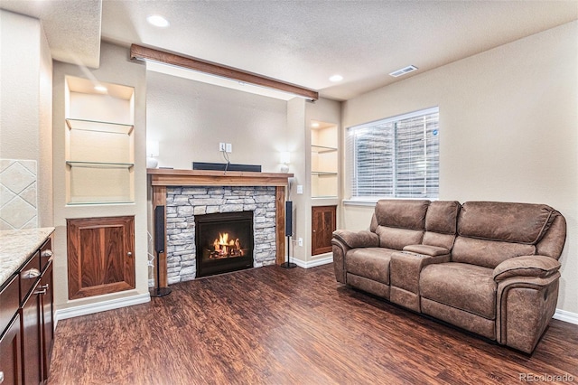 living room featuring dark hardwood / wood-style floors, a stone fireplace, built in features, and a textured ceiling