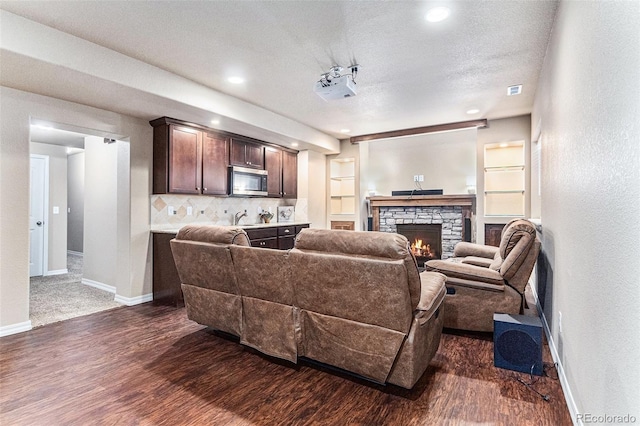 living room with dark wood-type flooring, a stone fireplace, sink, built in features, and a textured ceiling