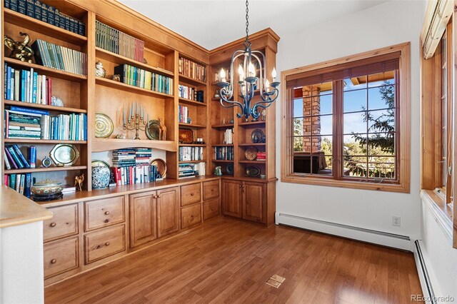 unfurnished office featuring light wood-type flooring, a baseboard radiator, and an inviting chandelier