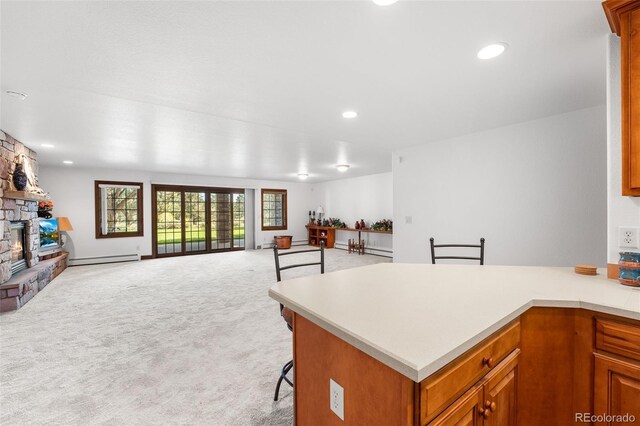 kitchen featuring a stone fireplace, light colored carpet, a kitchen breakfast bar, and baseboard heating