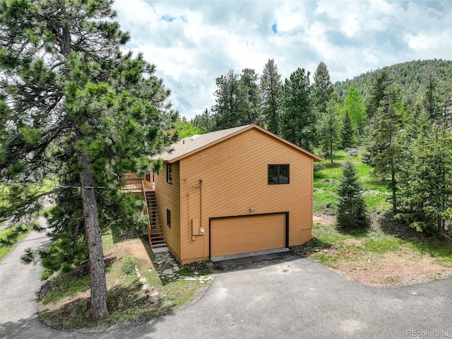 31150 Manitoba Dr, Evergreen, CO 80439 - view of home's exterior with driveway, an attached garage, a forest view, stairs, and a wooden deck