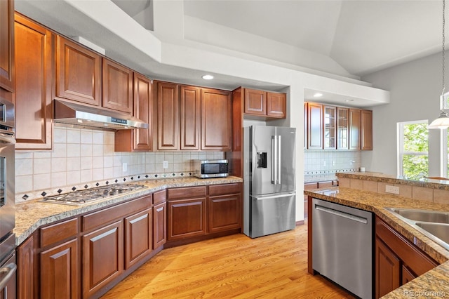 1513 Cannon Mountain Dr, Longmont, CO 80503 - kitchen with appliances with stainless steel finishes, under cabinet range hood, tasteful backsplash, light wood-type flooring, and decorative light fixtures