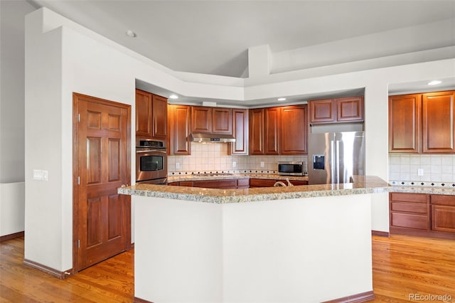1513 Cannon Mountain Dr, Longmont, CO 80503 - kitchen with appliances with stainless steel finishes, under cabinet range hood, light wood finished floors, and backsplash