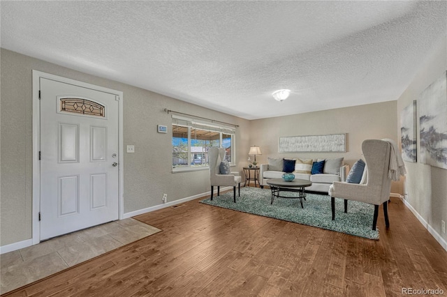 living room featuring wood finished floors, a textured ceiling, baseboards, and a textured wall