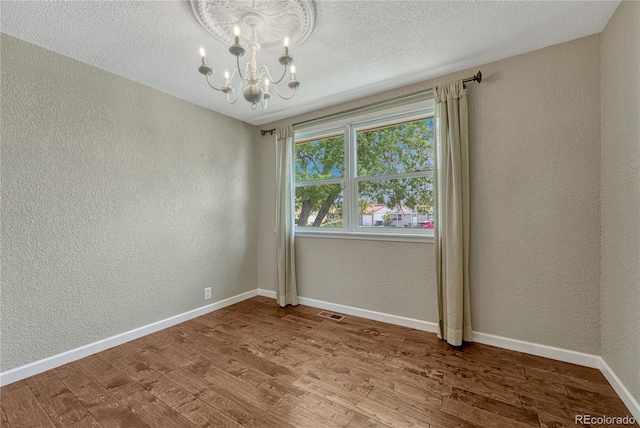 spare room with a textured wall, a chandelier, wood finished floors, baseboards, and a textured ceiling