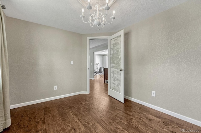 empty room with a textured wall, a chandelier, baseboards, dark wood-style floors, and a textured ceiling