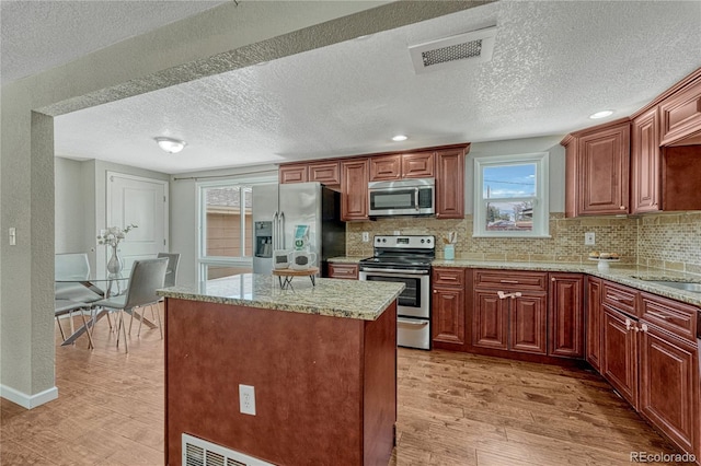 kitchen with stainless steel appliances, light wood-type flooring, a textured ceiling, tasteful backsplash, and a kitchen island