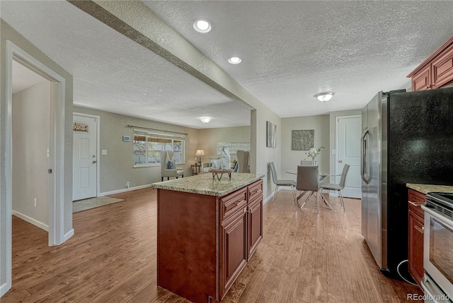 kitchen with wood finished floors, appliances with stainless steel finishes, a textured ceiling, baseboards, and open floor plan