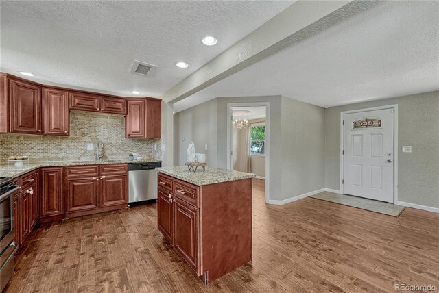 kitchen with stainless steel appliances, wood finished floors, a sink, a textured ceiling, and a chandelier