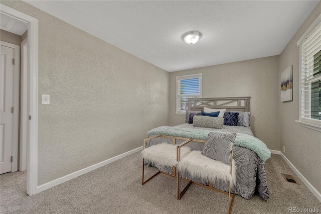 carpeted bedroom with a textured wall, multiple windows, and baseboards