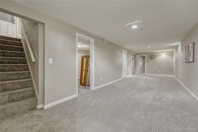 finished basement with carpet flooring, stairway, a textured ceiling, baseboards, and a textured wall