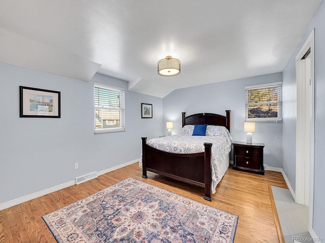 bedroom featuring lofted ceiling, baseboards, visible vents, and wood finished floors