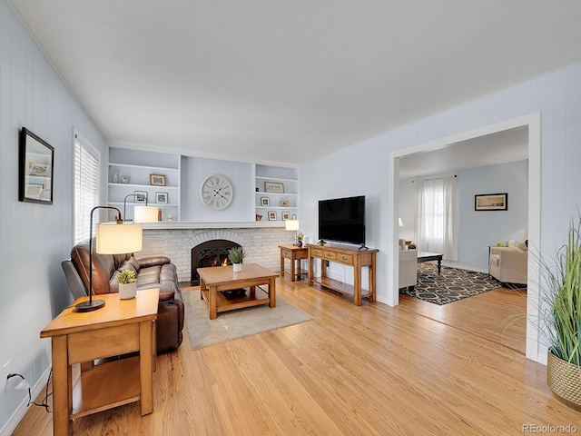 living room with a brick fireplace, built in shelves, baseboards, and light wood finished floors