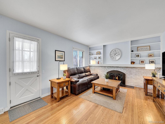 living area featuring built in shelves, a fireplace, visible vents, baseboards, and light wood finished floors