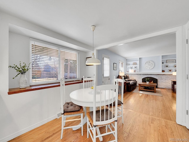 dining space featuring built in features, a fireplace, light wood-style flooring, and baseboards