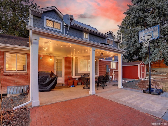 rear view of property with an outbuilding, a patio, a storage unit, and brick siding