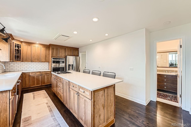 3695 E Dartmouth Ave, Denver, CO 80210 - kitchen with appliances with stainless steel finishes, dark wood finished floors, a kitchen island, tasteful backsplash, and light countertops