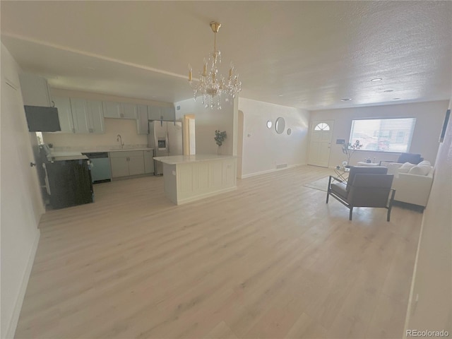 unfurnished living room with sink, a textured ceiling, light hardwood / wood-style flooring, and a chandelier