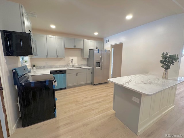 kitchen featuring sink, stainless steel appliances, light stone counters, kitchen peninsula, and light wood-type flooring