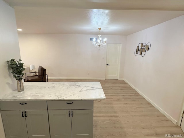 kitchen featuring decorative light fixtures, gray cabinetry, a chandelier, light stone countertops, and light hardwood / wood-style flooring