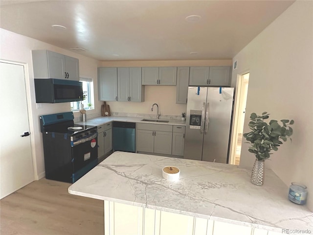 kitchen featuring light stone countertops, a peninsula, light wood-style flooring, a sink, and black appliances