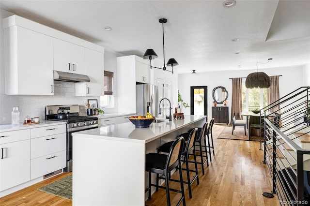 kitchen featuring appliances with stainless steel finishes, hanging light fixtures, an island with sink, white cabinets, and decorative backsplash