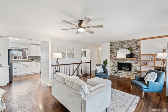 living room with a ceiling fan, a stone fireplace, and wood finished floors