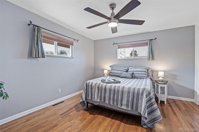 bedroom with multiple windows, wood finished floors, visible vents, and baseboards