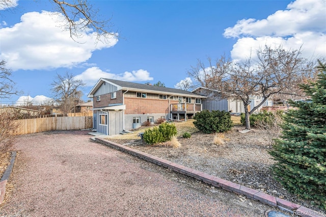 rear view of house featuring driveway, a wooden deck, fence, and brick siding