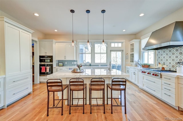 kitchen featuring pendant lighting, backsplash, wall chimney exhaust hood, an island with sink, and stainless steel gas cooktop