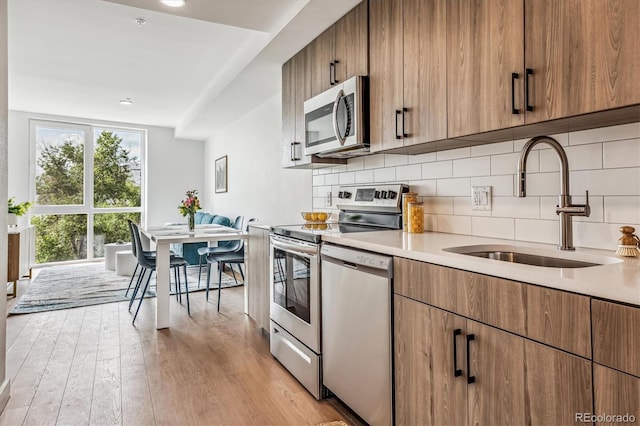 kitchen featuring light wood finished floors, a sink, tasteful backsplash, light countertops, and appliances with stainless steel finishes