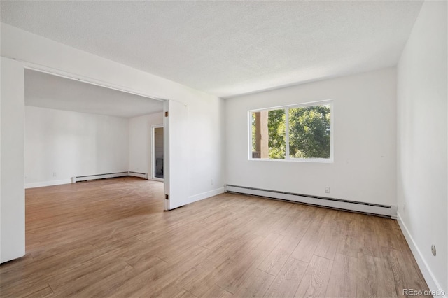 empty room with a textured ceiling, light wood-type flooring, and a baseboard heating unit