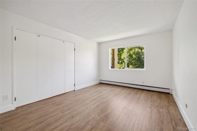 unfurnished bedroom featuring a textured ceiling, light wood-type flooring, a baseboard radiator, and a closet