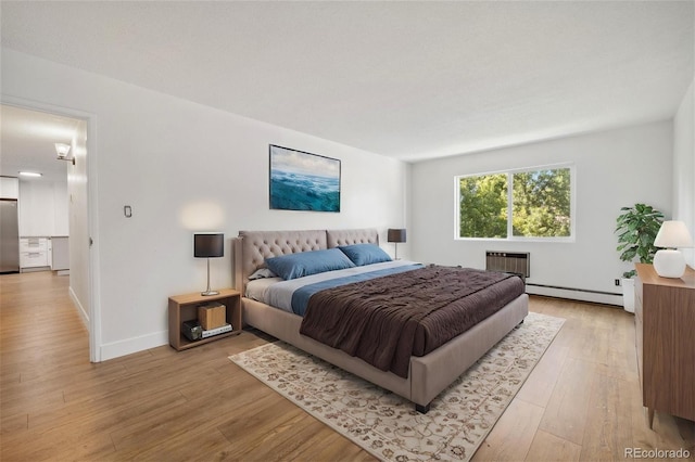 bedroom with a wall unit AC, light wood-type flooring, baseboard heating, and stainless steel refrigerator