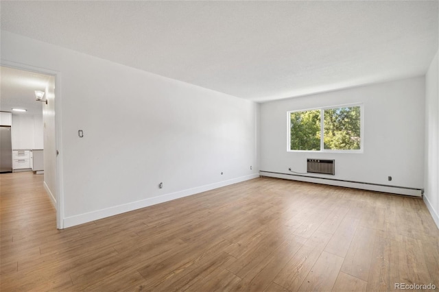 empty room with light hardwood / wood-style floors, a wall mounted air conditioner, and a baseboard heating unit