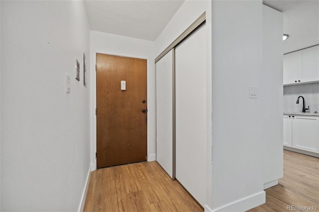 hallway featuring sink, light hardwood / wood-style floors, and a textured ceiling