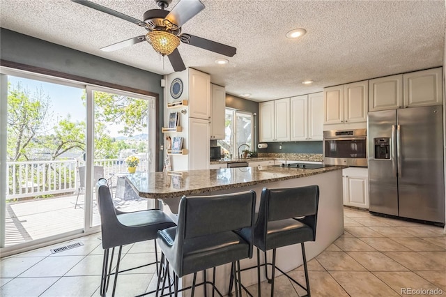 8150 W Calhoun Dr, Littleton, CO 80123 - kitchen featuring stainless steel appliances, a kitchen breakfast bar, dark stone counters, a ceiling fan, and a textured ceiling