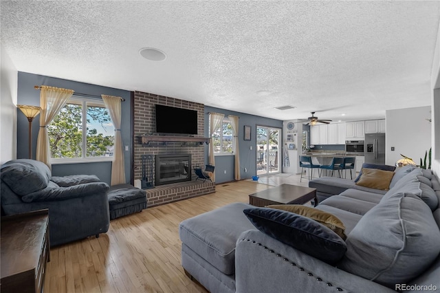 8150 W Calhoun Dr, Littleton, CO 80123 - living room featuring a textured ceiling, plenty of natural light, light wood-style flooring, a brick fireplace, and ceiling fan