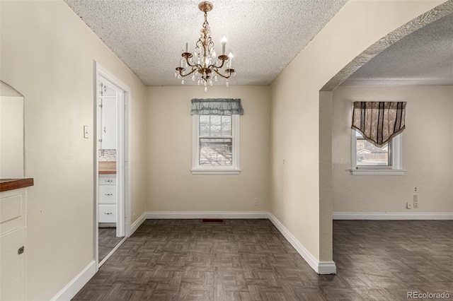 unfurnished dining area featuring a chandelier, a textured ceiling, and baseboards