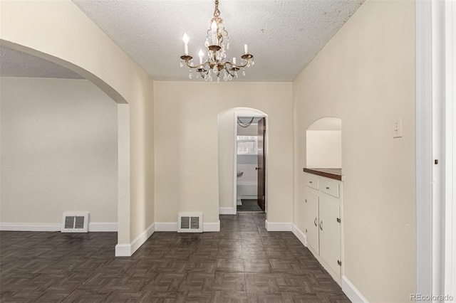 interior space featuring baseboards, visible vents, arched walkways, and a textured ceiling