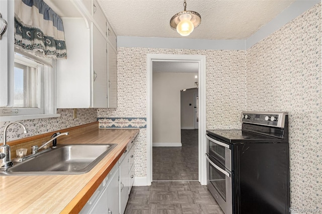 kitchen featuring wallpapered walls, white cabinets, range with two ovens, butcher block countertops, and a sink